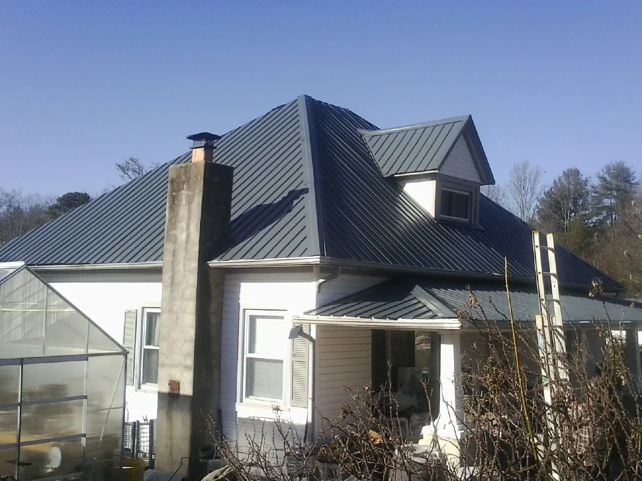 Dark blue standing seam metal roof on a white farmhouse with dormer — Slate & Tile Roof Repair by Roofing Brothers in Pioneer