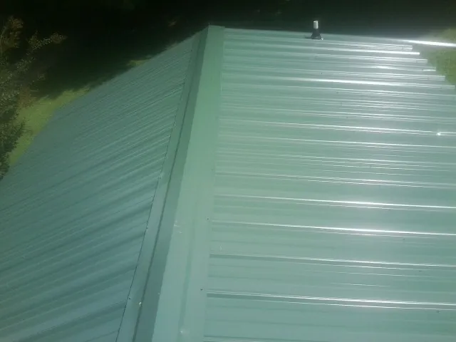 New green metal panels meeting at the ridge of a roof — Flat Roof Repair work by our crew in Pioneer