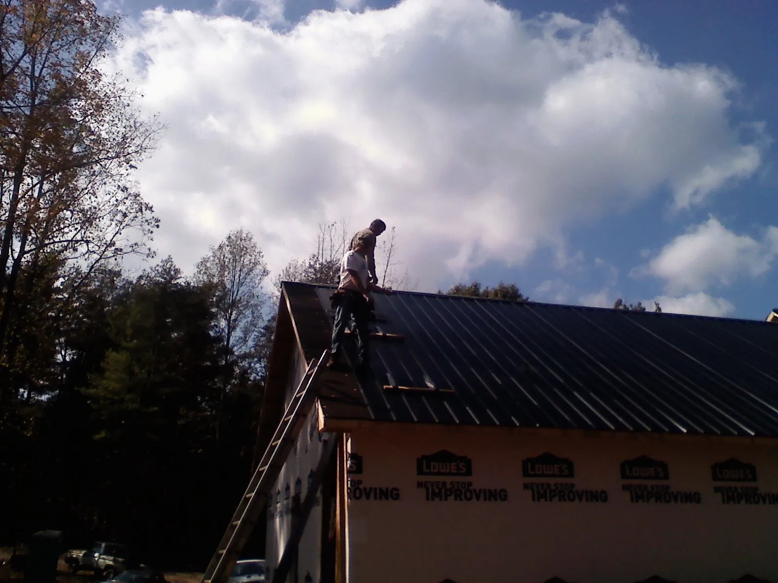 Roofer fastening dark metal panels high against a cloudy sky, from a Roof Inspection job in Pioneer