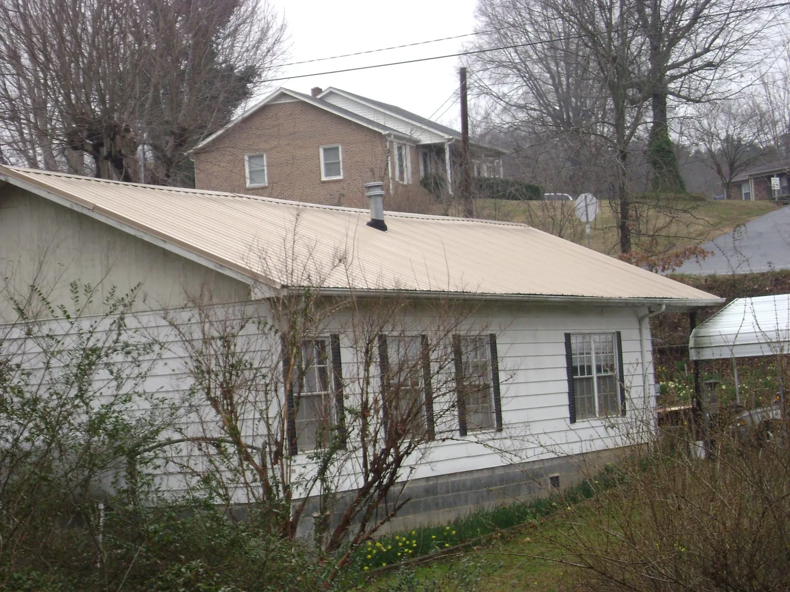 Tan metal roof on a white sided house set into a hillside — Commercial Roofing by Roofing Brothers in Pioneer