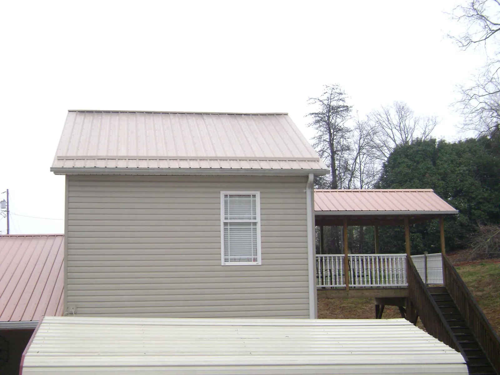 Tan metal roofs on a two story addition and attached porch, from a Roof Replacement job in Pioneer